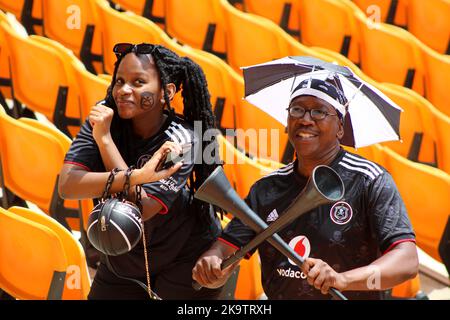 Belle femme fan de football souriant, Orlando Pirates fan portant un kit de football, et homme portant un chapeau de parapluie Banque D'Images