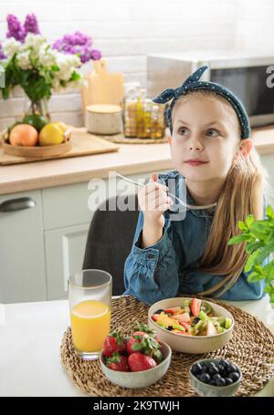 Une alimentation saine à la maison. Une petite fille mignonne mange de la salade de fruits Banque D'Images