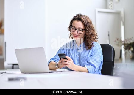 Jeune femme d'affaires utilisant un smartphone travaillant au bureau assis au bureau. Banque D'Images