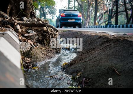 11 février 2022 Dehradun Inde. Le drainage latéral de la route s'écoule avec le trafic hors foyer en arrière-plan. Banque D'Images