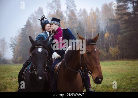 Homme et femme en 19th siècle, les costumes de style Empire posent à cheval, homme embrassant une femme sur la joue. Banque D'Images