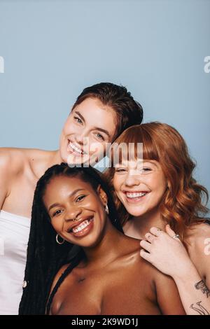 Des femmes heureuses avec différentes tons de peau souriant à l'appareil photo dans un studio. Groupe de jeunes femmes confiantes de corps embrassant leur beauté naturelle. Trois dbo Banque D'Images