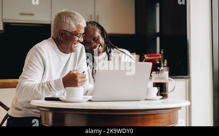 Un couple de personnes âgées joyeux souriant en utilisant un ordinateur portable ensemble. Couple mature recherchant leurs options de retraite en ligne. Coupe sénior sans souci Banque D'Images