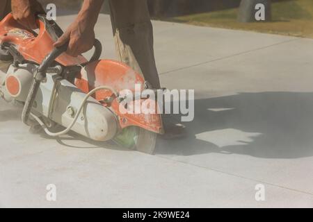 Un employé d'une entreprise de construction coupe des trottoirs en béton avec une scie à disque diamant Banque D'Images