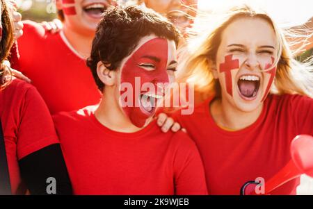 Les fans de football de sport rouge crient tout en soutenant leur équipe hors du stade - concentrez-vous sur le visage de fille centrale Banque D'Images