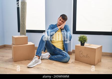 Jeune hispanique assis sur le sol dans une nouvelle maison dormant fatigué rêvant et posant avec les mains ensemble tout en souriant avec les yeux fermés. Banque D'Images