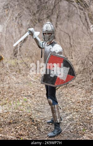 Noble guerrier. Portrait d'un guerrier ou chevalier médéival en armure et casque avec bouclier et épée posé isolé sur fond sombre. Banque D'Images