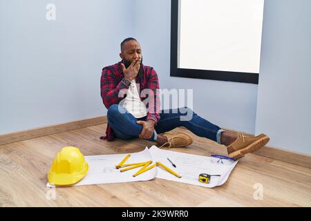 Afro-américain homme assis sur le sol dans une nouvelle maison regardant les plans lassés latent fatigué couvrant la bouche avec la main. Agité et somnolence. Banque D'Images