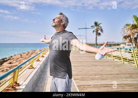 Homme hispanique d'âge moyen portant des vêtements de sport respirant au bord de la mer Banque D'Images