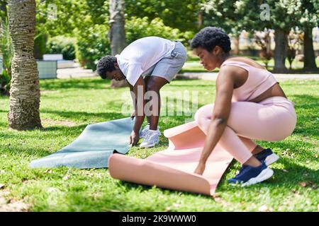 Un couple afro-américain souriant et confiant a mis le tapis de yoga sur le sol du parc Banque D'Images
