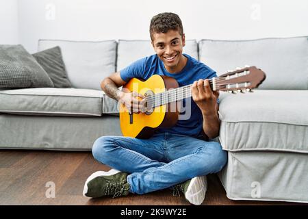 Jeune homme hispanique jouant de la guitare assis sur le sol à la maison Banque D'Images