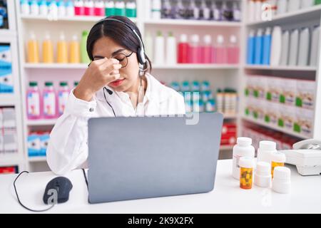 Jeune femme arabe travaillant à la pharmacie drugstore en utilisant ordinateur portable fatigué frottant nez et yeux sensation de fatigue et de maux de tête. Stress et frustration concept. Banque D'Images
