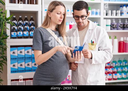 Homme et femme pharmacien et cliente enceinte regardant un écran de smartphone à la pharmacie Banque D'Images