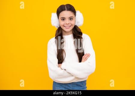 Belle jeune fille en hiver chaud cache-oreilles et un pull chaud. Un enfant sur un arrière-plan jaune isolé. Un visage heureux, positif et souriant Banque D'Images