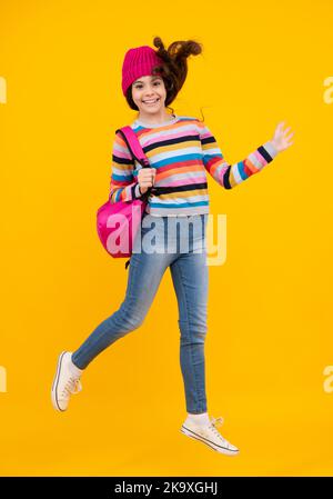 Vacances scolaires d'hiver. Retour à l'école. Adolescente avec chapeau chaud et chandail sur fond jaune isolé studio. École d'hiver. Heureux Banque D'Images