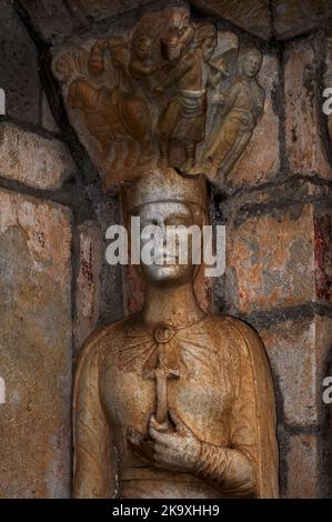 Sainte-Hélène, impératrice romaine et mère du premier empereur chrétien, Constantine I, tient un crucifix tandis que la capitale sculptée ci-dessus dépeint sa quête pour trouver de précieuses reliques de Crucifixion à Jérusalem. Statue de pilier romane datant de 12th ans et capitale sculptée dans le portail nord de l'église pyrénéenne contenant un fragment de la vraie Croix, la Basilique Saint-Just à Valcabrère, Occitanie, France. Banque D'Images