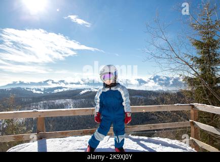 joyeux garçon dans un casque, des lunettes, une combinaison bleue à la station de ski sur fond de paysage de montagne magnifique. Animations hivernales pour les enfants. Banque D'Images