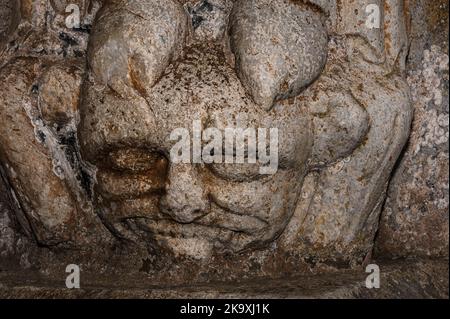 Les bons triomphes du mal : un visage grotesque avec une rangée de dents massives, symboliquement écrasées sous les pieds de Sainte-Hélène de Constantinople. Dans le portail nord de la fin de 1100s AD roman Basilique Saint-Just, consacré en 1200 AD à Valcabrère, Occitanie, sud-ouest de la France. Banque D'Images