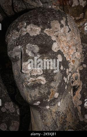 Le visage lichen-incrusté de l'élève de sept ans Just ou Jutus, martyrisé avec le frère aîné Pastor par les Romains en Espagne pour avoir dénoncé leur religion. Détail de la statue de pilier médiévale en basilique Saint-Just à Valcabrère, Occitanie, France. Les capitales sculptées au-dessus des deux statues des garçons montrent leur arrestation, torture et exécution. Banque D'Images