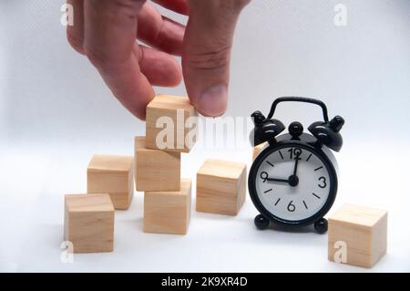 Cubes en bois vierges et réveil noir sur fond blanc avec espace personnalisable pour le texte ou les idées. Banque D'Images
