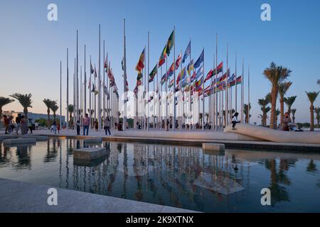 Vue de la corniche de Doha au coucher du soleil montrant les drapeaux des pays participants et la fontaine en premier plan avec les gens qui célèbrent. Préparation du Qatar pour la FIFA Banque D'Images