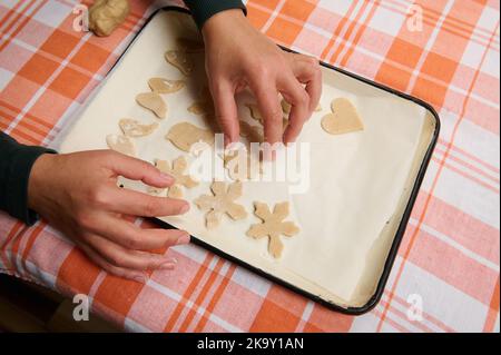 Gros plan des mains du chef en plaçant des biscuits de pâte sculptés sur une plaque de cuisson, avant de cuire au four. Pain d'épice de Noël Banque D'Images