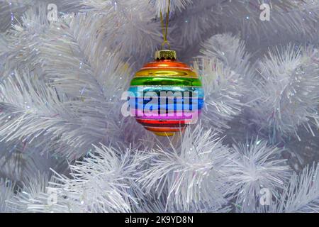 Boule de Noël couleur arc-en-ciel en verre brillant, boule accrochée à un sapin de noël artificiel blanc. Le concept de la fête, Noël, symbole de la Banque D'Images