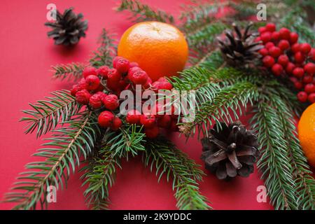 L'esprit de Noël, les décorations de la nature : branches de sapin, cônes, baies de Rowan rouge vif et mandarines sur fond rouge. Banque D'Images