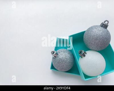 Boîtes de bijoux turquoise à l'intérieur de laquelle est une brillante boules de Noël blanc et couleur argent sur la droite. Arrière-plan blanc. Copier l'espace. Banque D'Images