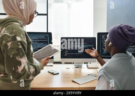 Un jeune ingénieur INFORMATIQUE afro-américain confiant présente des données décodées sur écran d'ordinateur à une collègue féminine du hijab Banque D'Images