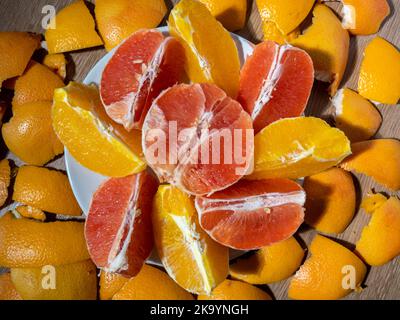 oranges et pamplemousses coupées en morceaux sur une assiette blanche. À côté de lui se trouve le pelage après la cueillette des fruits. Vitamines et repas pour une alimentation saine Banque D'Images