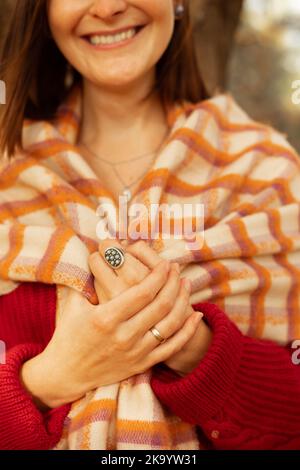 Portrait en gros plan de femme mignonne souriante avec anneaux élégants, en chandail rouge confortable, recouvert d'une couverture chaude à carreaux. Une jeune femme attrayante est à l'entrée Banque D'Images