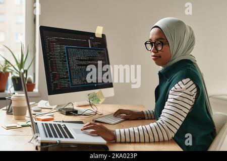 Vue latérale d'un jeune stagiaire ou d'un développeur de logiciels professionnel touchant le pavé tactile d'un ordinateur portable tout en regardant des informations en ligne Banque D'Images