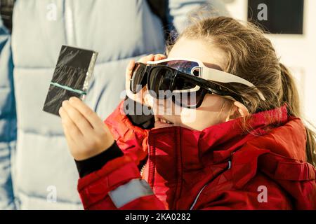 Enfant regardant l'éclipse solaire avec verre filtre sombre et plusieurs lunettes de soleil, drôle petite fille regardant l'éclipse du soleil. Affichage enfant d'eclipse dans le ciel. Conc Banque D'Images