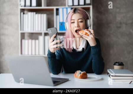 Une jeune femme asiatique excitée qui porte un casque joue avec son smartphone. Gamer avec Internet Banque D'Images