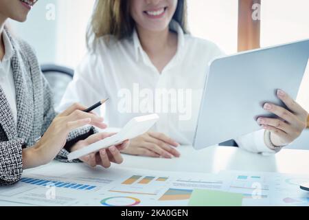 Deux jeunes femmes d'affaires asiatiques utilisant leurs tablettes informatiques avec des calculatrices et des documents pour planifier des stratégies de marketing et des investissements à tirer profit Banque D'Images