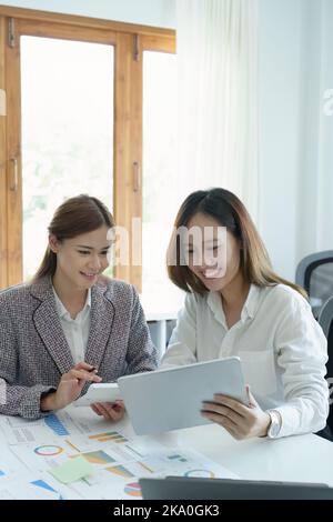 Un portrait de deux jeunes femmes d'affaires asiatiques utilisant leur tablette informatique avec des calculatrices et des documents pour planifier des stratégies et des investissements marketing Banque D'Images