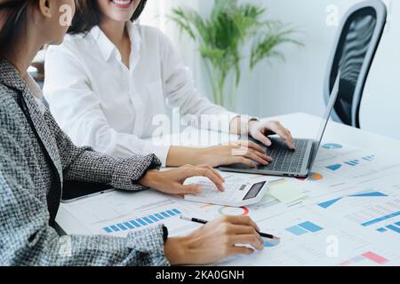 Deux jeunes femmes d'affaires asiatiques utilisant leurs tablettes informatiques avec des calculatrices et des documents pour planifier des stratégies de marketing et des investissements à tirer profit Banque D'Images