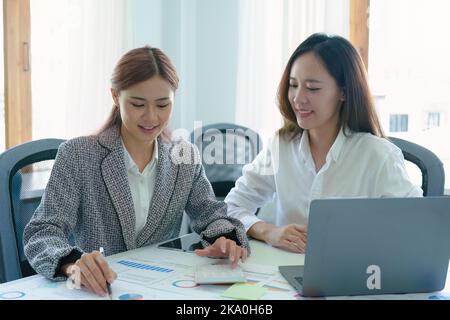 Deux jeunes femmes d'affaires asiatiques utilisant leurs tablettes informatiques avec des calculatrices et des documents pour planifier des stratégies de marketing et des investissements à tirer profit Banque D'Images