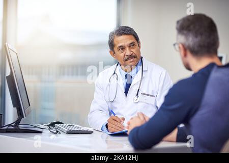 Vous avez un médecin qui s'en soucie. Un homme joyeux et mature s'est assis à son bureau tout en consultant un patient à l'intérieur d'un hôpital pendant la journée. Banque D'Images