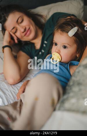 Maman aimante avec le sourire couché sur le lit avec son adorable fille de babu appréciant des moments doux de bonheur. Lit confortable avec bébé, capture Banque D'Images