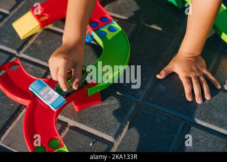 Vue rapprochée des mains d'un petit garçon jouant avec des blocs de construction en plastique coloré à l'arrière-cour de la maison, assis sur le sol. Jeux créatifs pour Banque D'Images