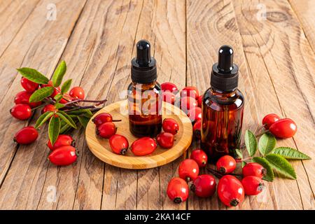 deux flacons cosmétiques avec pipette et produit biologique à base d'huile de rosehip sur fond de bois parmi les baies de rosehip mûres. vue avant Banque D'Images