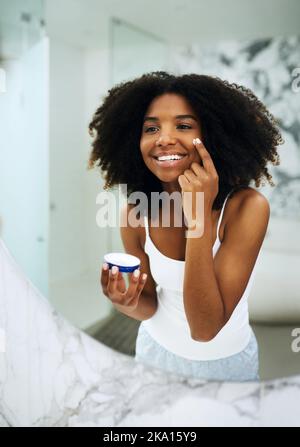 Une peau claire est accompagnée d'une routine. Une jeune femme attrayante appliquant un hydratant sur son visage à la maison. Banque D'Images