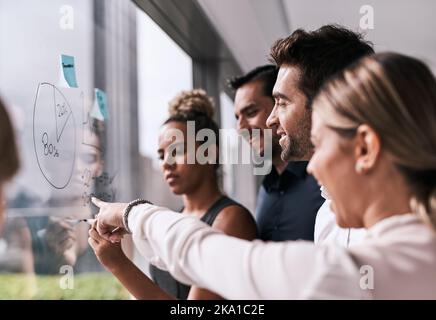 Un groupe d'hommes et de femmes d'affaires remue-méninges sur un mur de verre dans un bureau. Banque D'Images