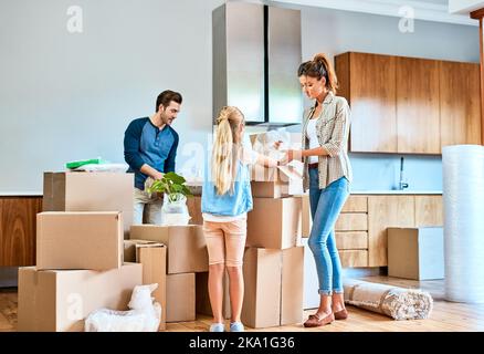 Toute la famille aide à la maison. Une jeune famille ciblée travaillant ensemble et déballant des boîtes dans leur nouvelle maison à l'intérieur pendant la journée. Banque D'Images