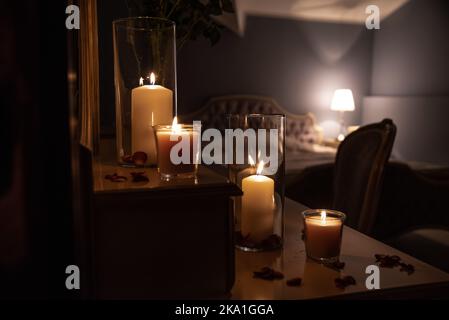 Le pot en verre avec des bougies allumées illumine la pièce, créant une atmosphère romantique et chaleureuse dans la chambre rétro avec une belle décoration en arrière-plan. Banque D'Images