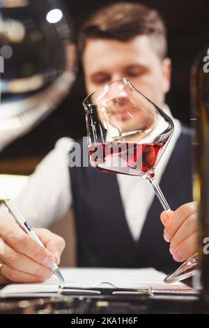 Le responsable du vin tient le verre de vin avec la boisson rouge, écrit un commentaire. Banque D'Images