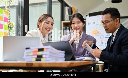 Les hommes d'affaires asiatiques du millénaire, professionnels et joyeux, ont une réunion informelle pour vérifier les résultats financiers de leur entreprise avant d'être présents Banque D'Images