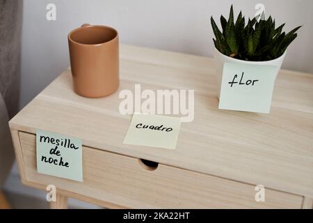 Vue rapprochée d'une table de nuit en bois avec une tasse de café et une plante locale verte dans un pot à fleurs et des autocollants en papier-note avec des mots espagnols Banque D'Images
